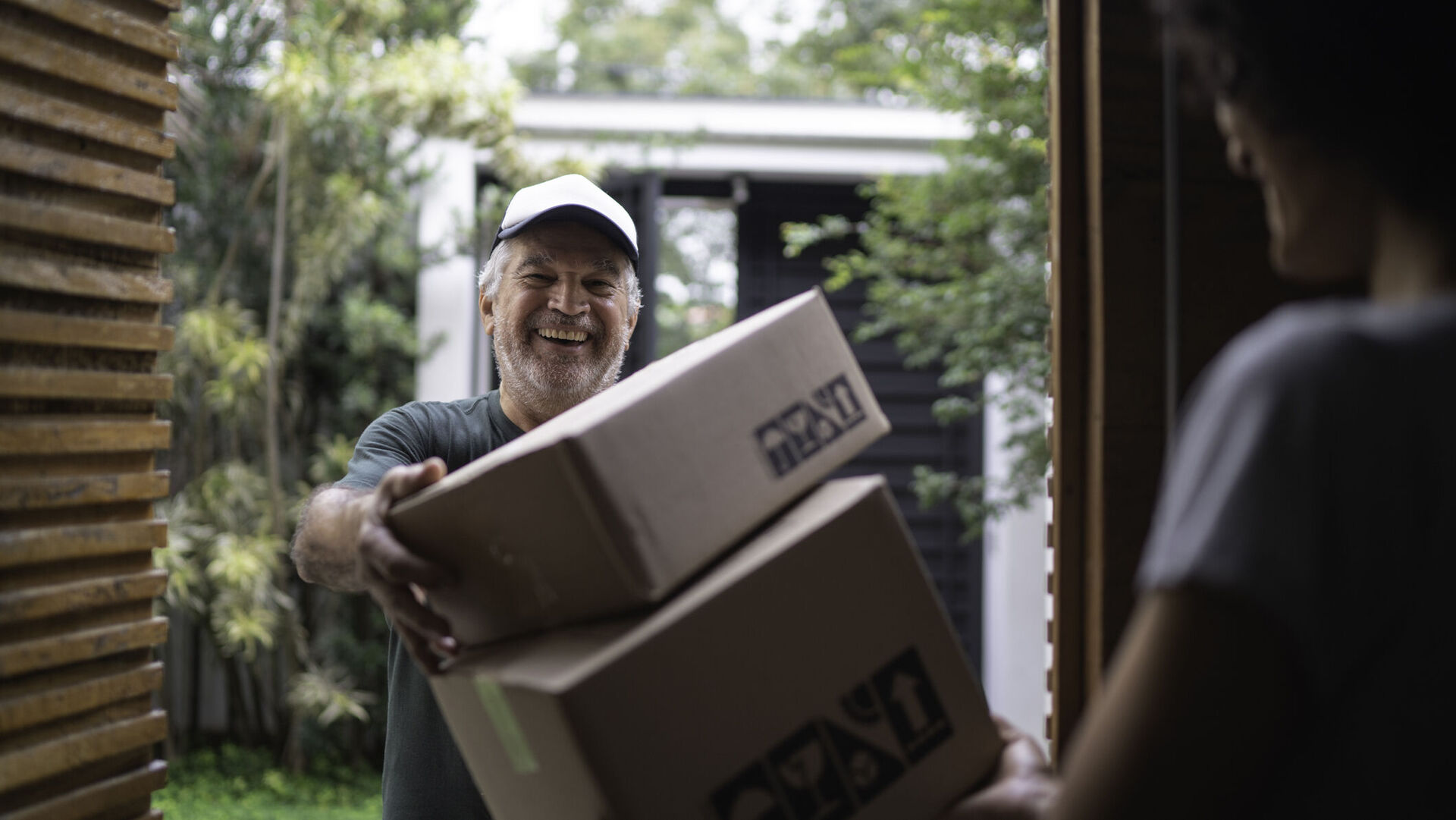 Ein Paketdienstleister liefert an der Haustür Pakete an einen jungen Mann.