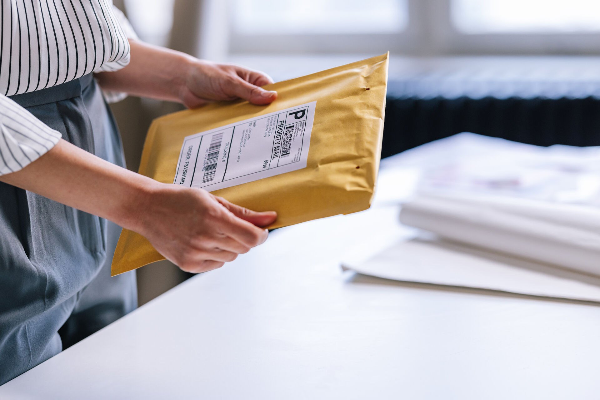 A woman holds a package with a printed shipping label in her hands.